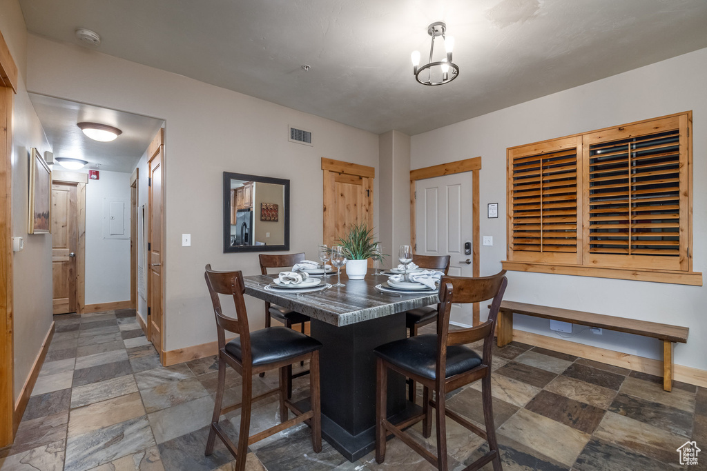 Dining room with stone finish flooring, visible vents, a chandelier, and baseboards