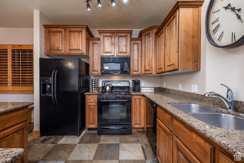 Kitchen with dark stone countertops, stone finish floor, brown cabinets, black appliances, and a sink