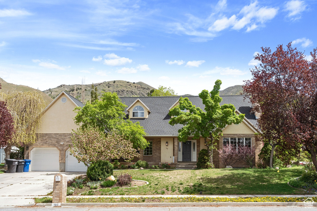 View of front of house featuring concrete driveway, brick siding, a mountain view, and a front lawn