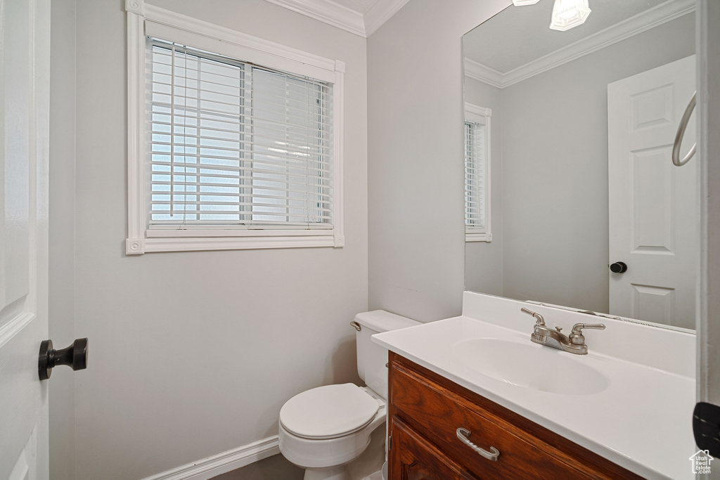 Half bath featuring baseboards, ornamental molding, toilet, and vanity