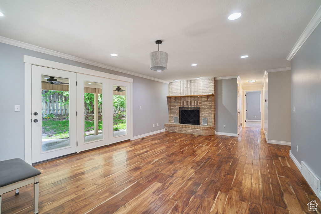 Unfurnished living room featuring hardwood / wood-style floors, a fireplace, visible vents, and crown molding
