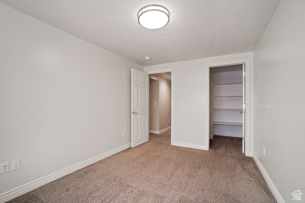 Unfurnished bedroom with a walk in closet, baseboards, a closet, and carpet