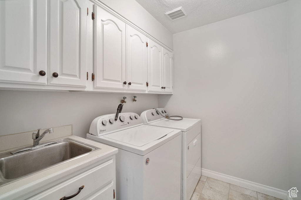 Clothes washing area featuring washer and dryer, cabinet space, a sink, baseboards, and visible vents
