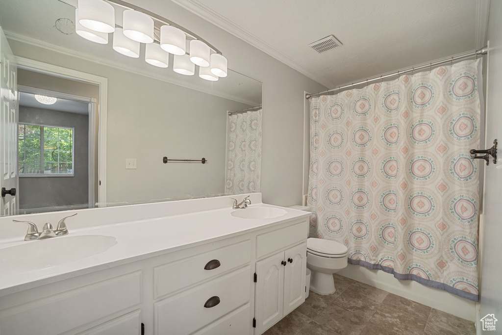 Bathroom with double vanity, toilet, crown molding, and a sink