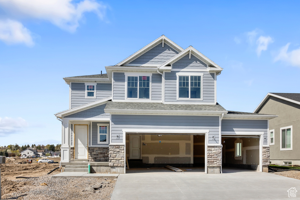 Craftsman-style house with driveway, a garage, a shingled roof, and stone siding