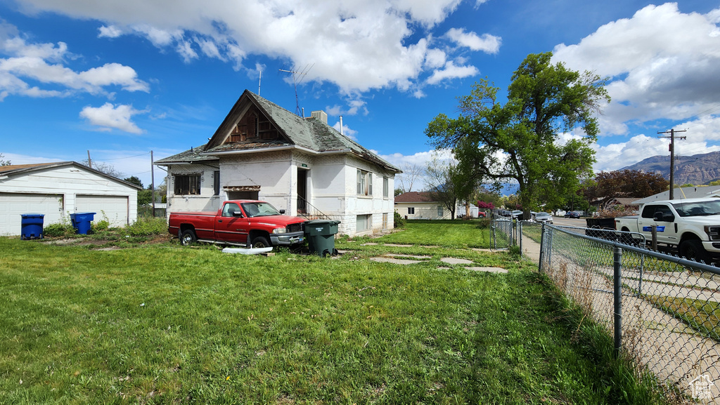 View of property exterior featuring a detached garage, fence, and a lawn