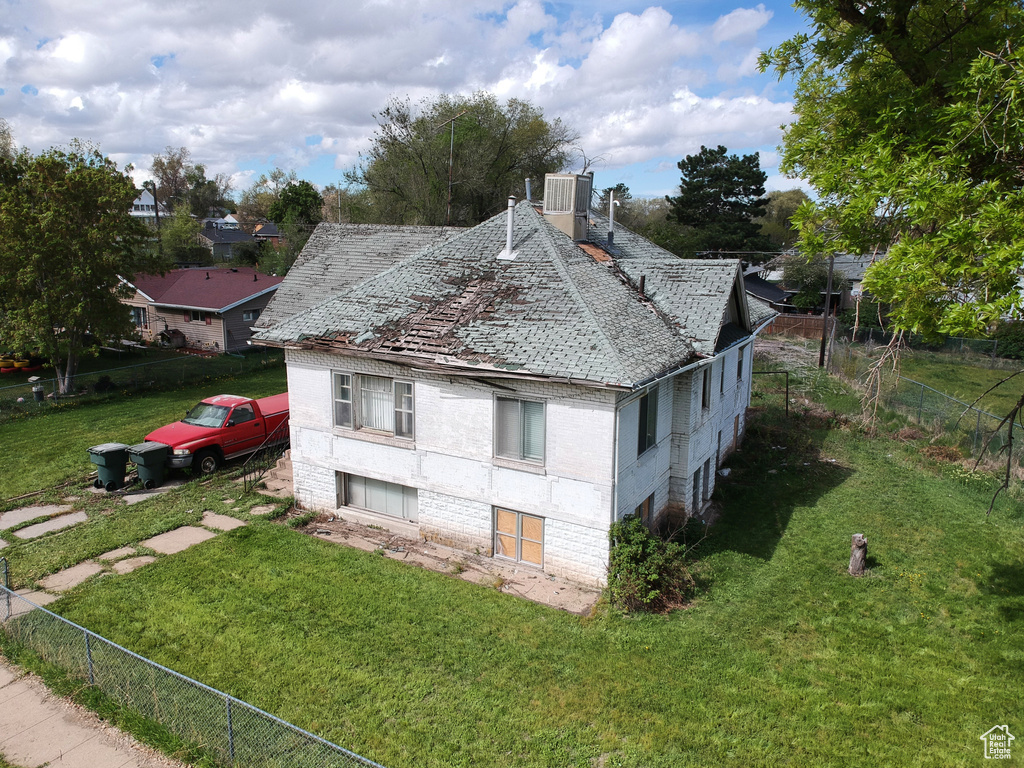 View of side of property with brick siding, fence, a yard, and roof with shingles