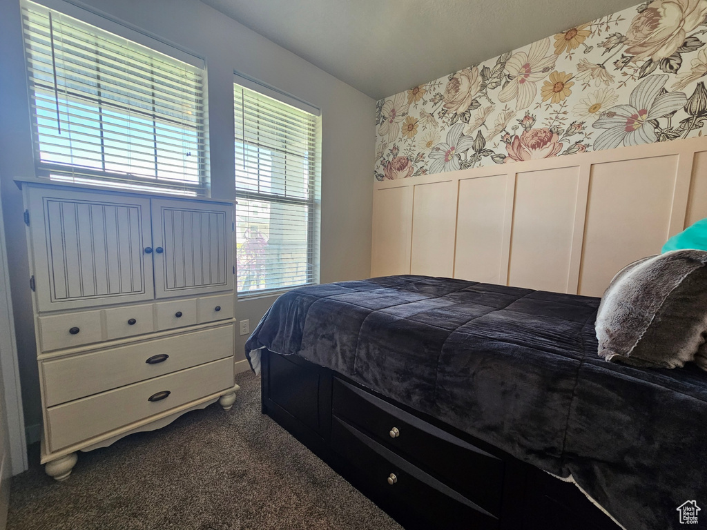 Bedroom with dark colored carpet, wainscoting, a decorative wall, and wallpapered walls
