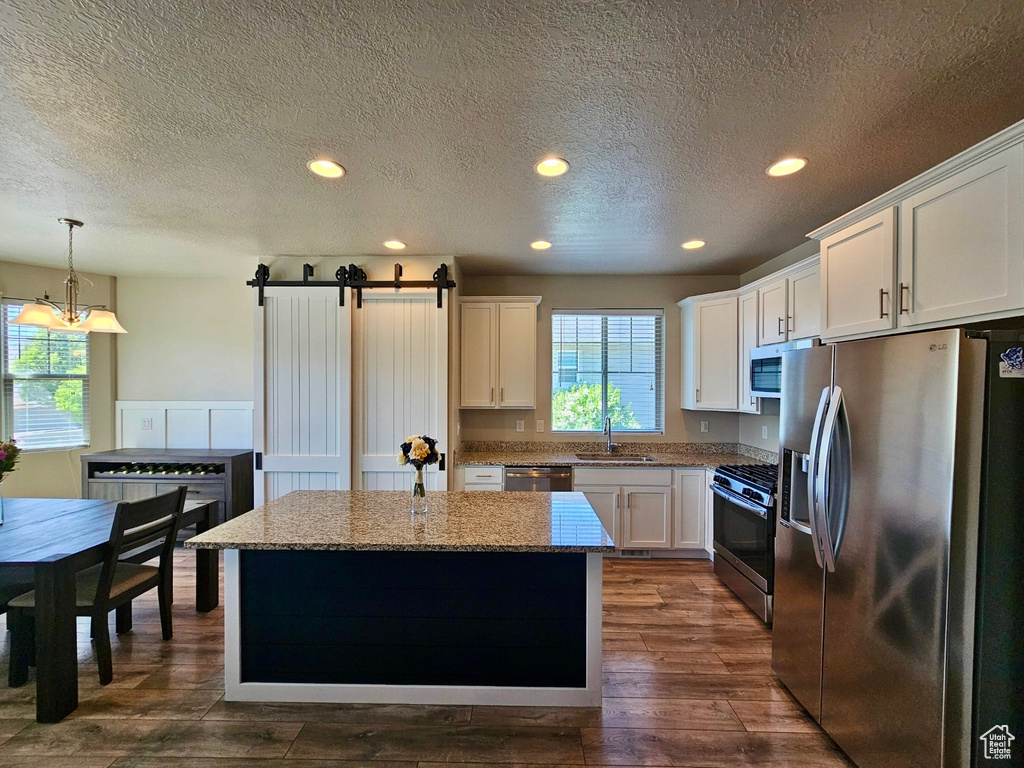 Kitchen with a kitchen island, a barn door, white cabinetry, a sink, and appliances with stainless steel finishes