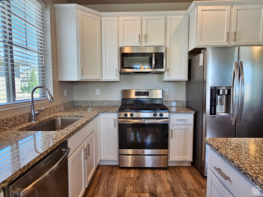 Kitchen featuring dark wood-style flooring, appliances with stainless steel finishes, light stone countertops, a sink, and white cabinets