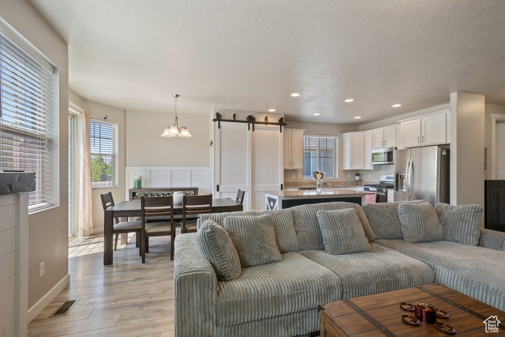 Living room with an inviting chandelier, a barn door, light wood-style flooring, recessed lighting, and visible vents