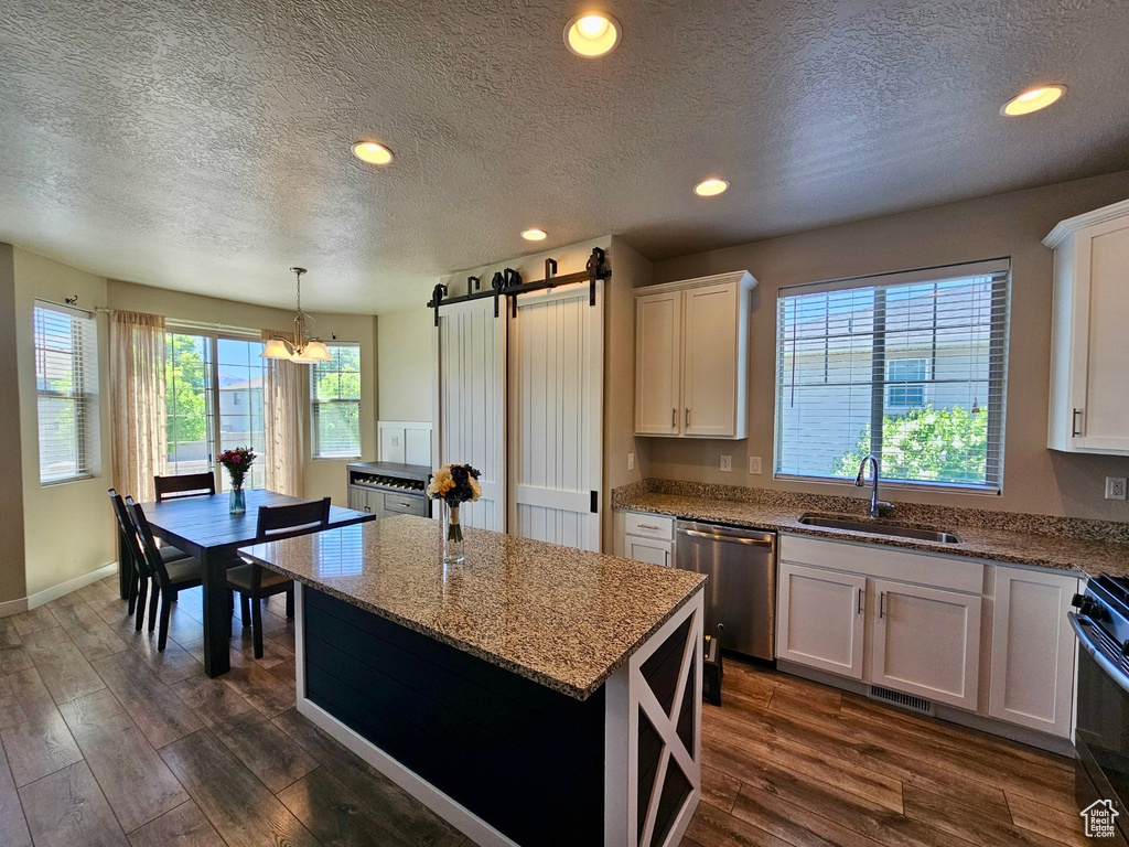 Kitchen with a textured ceiling, stainless steel dishwasher, a barn door, a sink, and dark wood-type flooring
