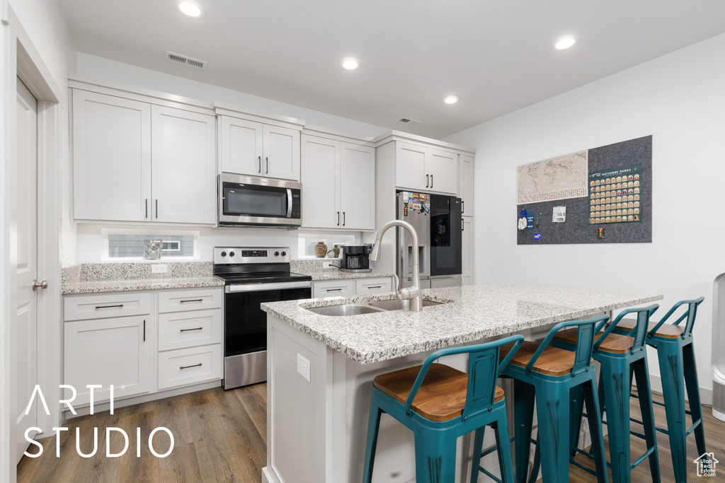 Kitchen with stainless steel appliances, a kitchen bar, a sink, visible vents, and dark wood-type flooring