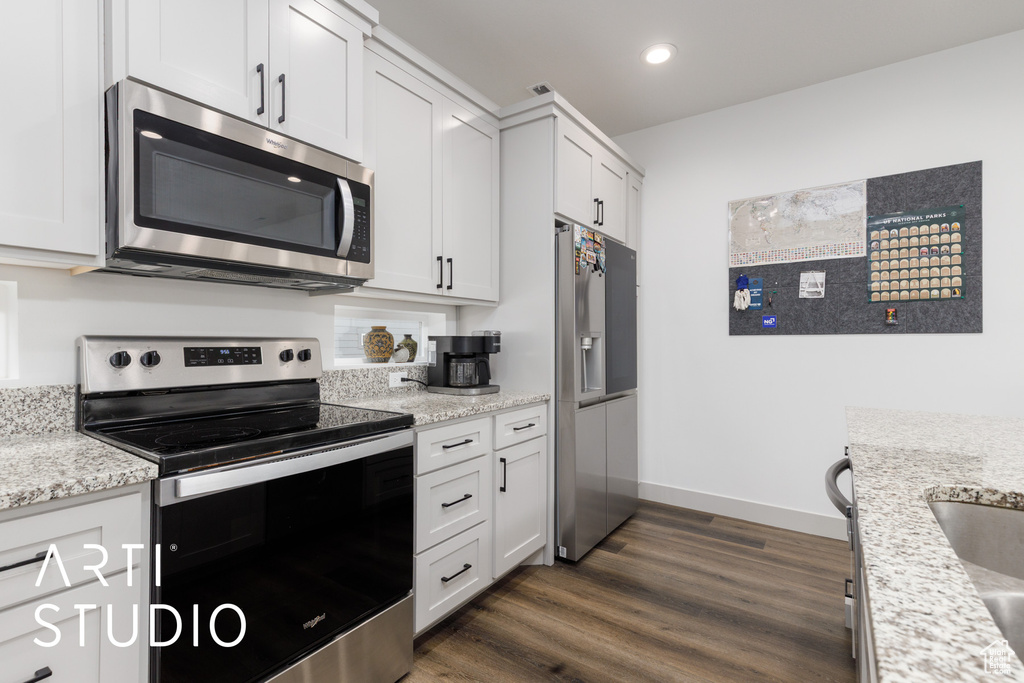 Kitchen with dark wood-style floors, recessed lighting, light stone countertops, white cabinetry, and appliances with stainless steel finishes
