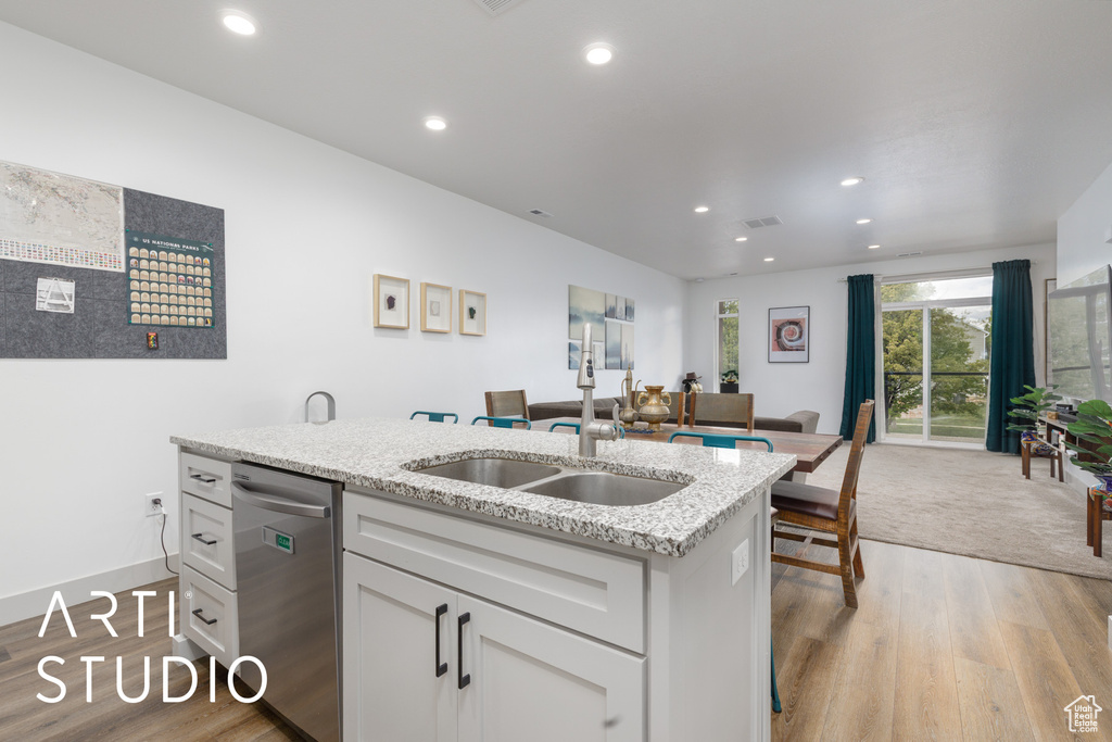 Kitchen featuring light wood-type flooring, stainless steel dishwasher, white cabinets, and a sink