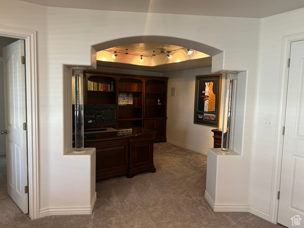 Hall featuring carpet floors, baseboards, a tray ceiling, and arched walkways