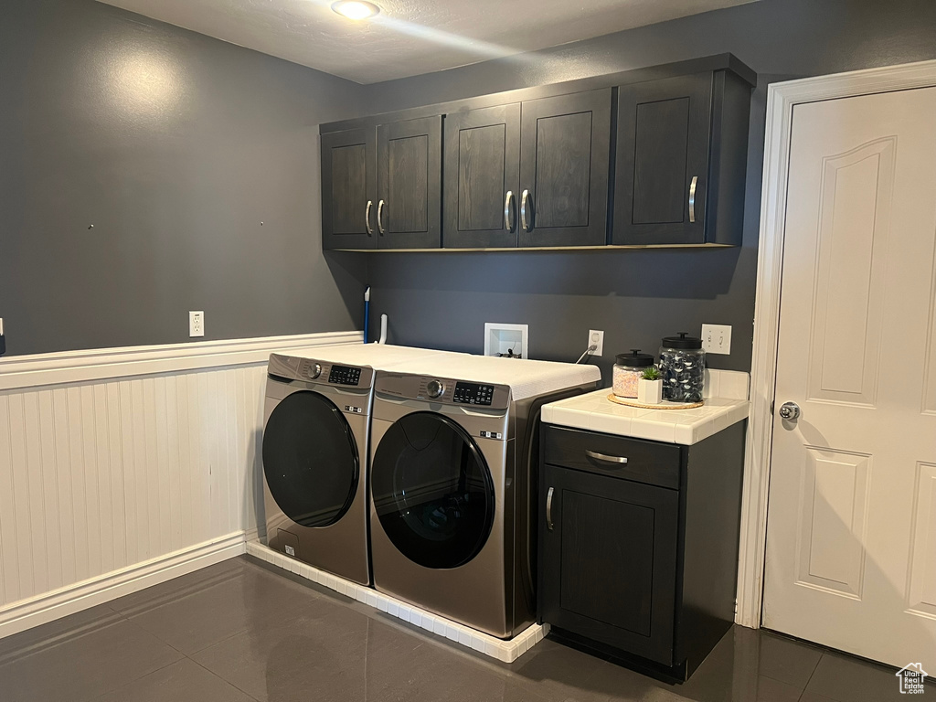 Clothes washing area featuring tile patterned floors, washer and dryer, a wainscoted wall, and cabinet space