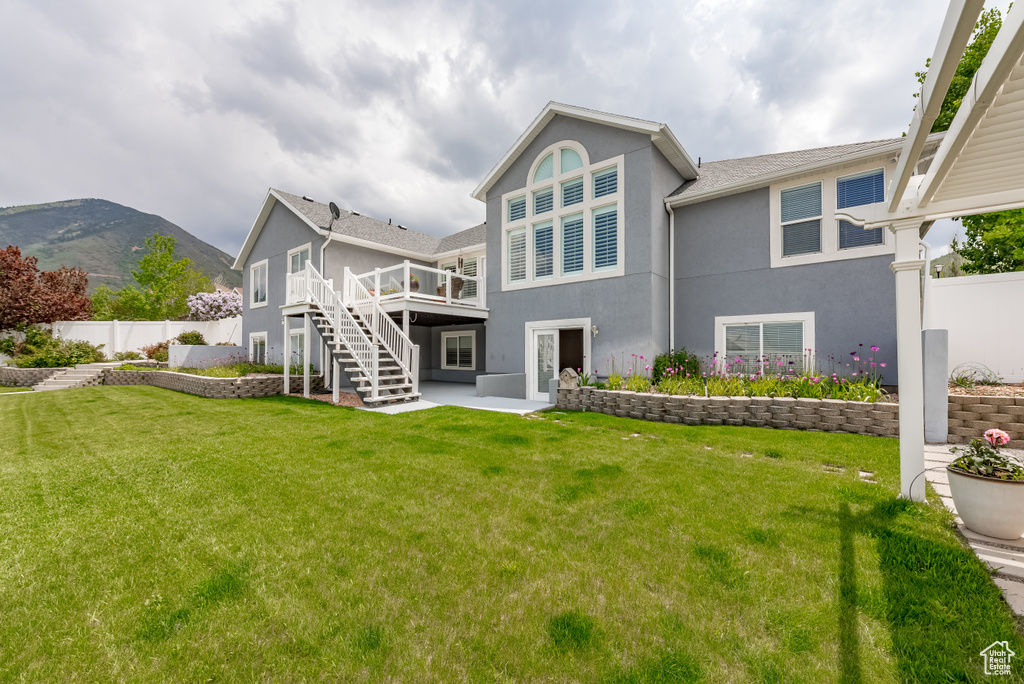 Back of property with stairway, a lawn, a deck, stucco siding, and fence