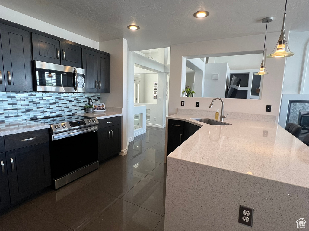 Kitchen featuring tasteful backsplash, dark tile patterned flooring, stainless steel appliances, dark cabinetry, and a sink
