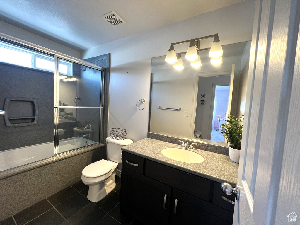 Bathroom with tile patterned flooring, toilet, vanity, visible vents, and bath / shower combo with glass door