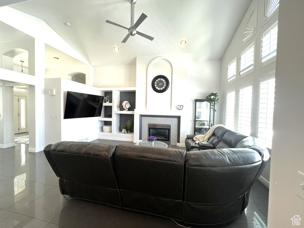 Living area featuring baseboards, a fireplace, a ceiling fan, high vaulted ceiling, and tile patterned flooring