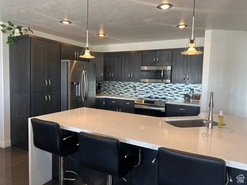 Kitchen featuring light stone countertops, a sink, a kitchen bar, backsplash, and appliances with stainless steel finishes