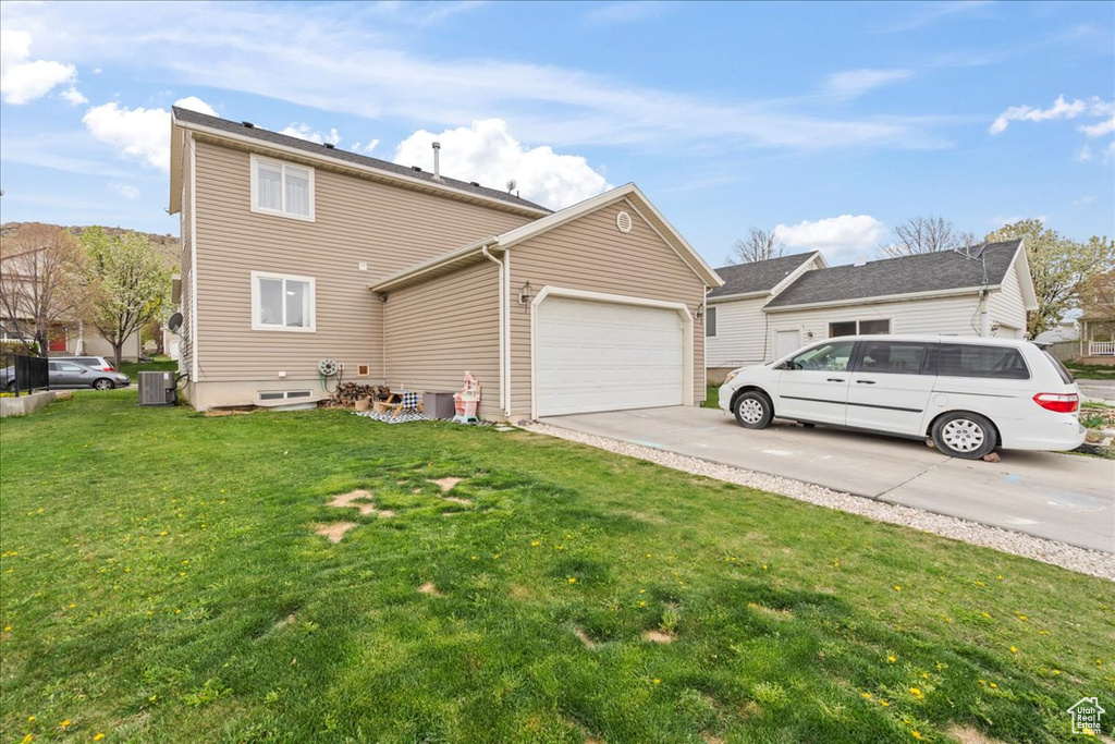 Exterior space with a garage, a yard, concrete driveway, and central air condition unit