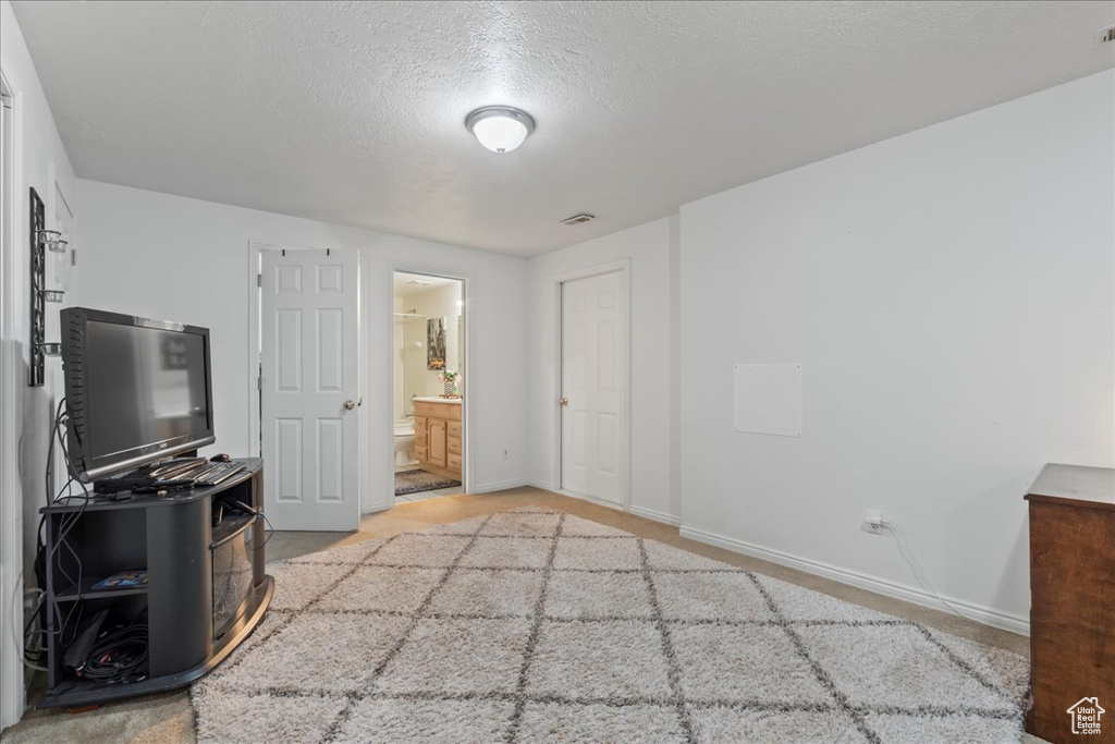 Unfurnished bedroom featuring a textured ceiling, visible vents, baseboards, light carpet, and ensuite bath