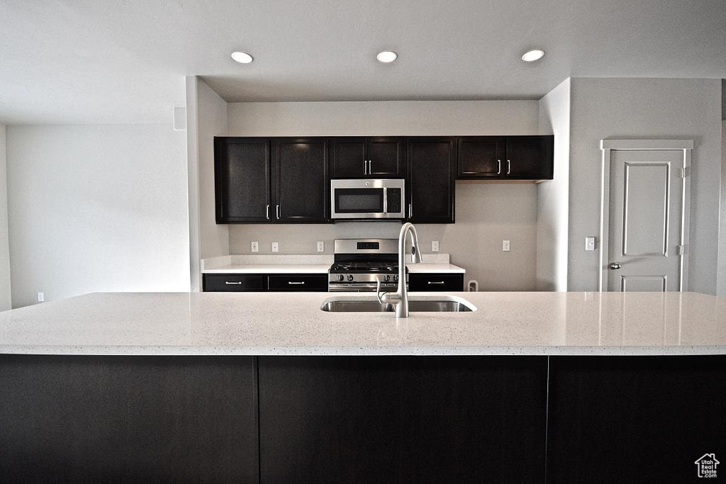 Kitchen featuring recessed lighting, a sink, dark cabinetry, appliances with stainless steel finishes, and an island with sink