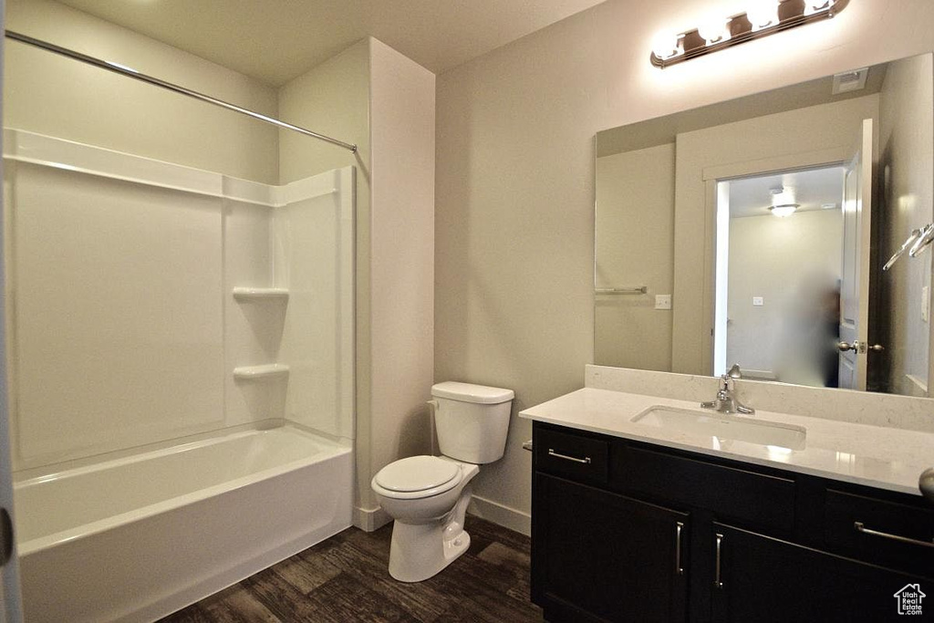Bathroom featuring wood finished floors, toilet, shower / bathtub combination, vanity, and baseboards