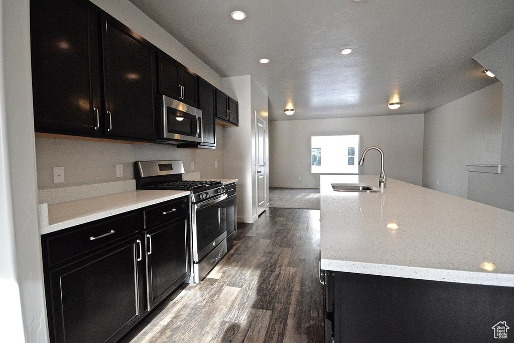 Kitchen with dark cabinetry, a sink, appliances with stainless steel finishes, and dark wood finished floors
