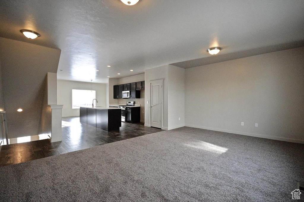 Unfurnished living room featuring dark carpet, a sink, recessed lighting, and baseboards