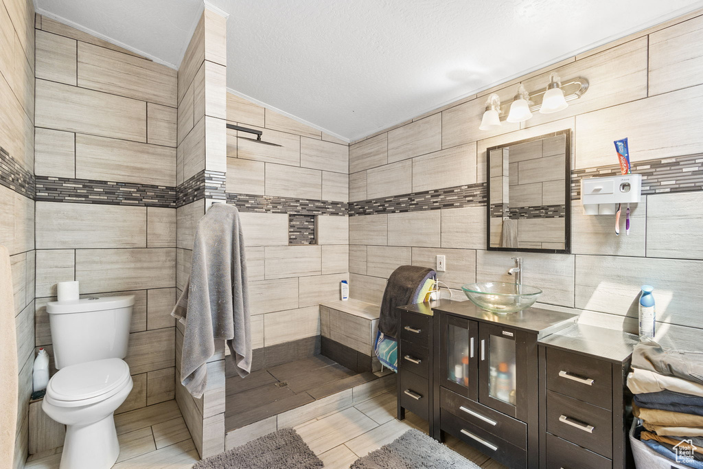 Bathroom featuring tile walls, vanity, toilet, and lofted ceiling