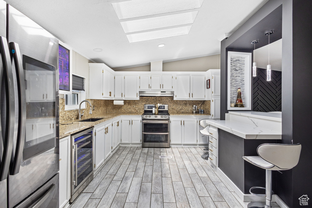 Kitchen with a sink, beverage cooler, stainless steel appliances, backsplash, and lofted ceiling with skylight
