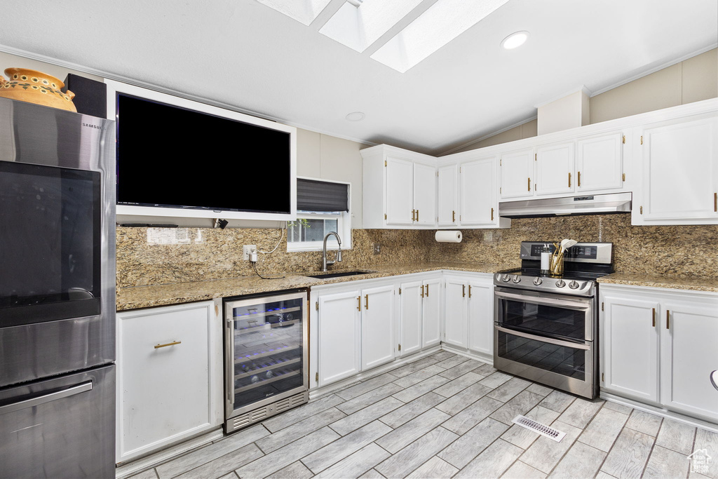 Kitchen with appliances with stainless steel finishes, a sink, beverage cooler, backsplash, and under cabinet range hood