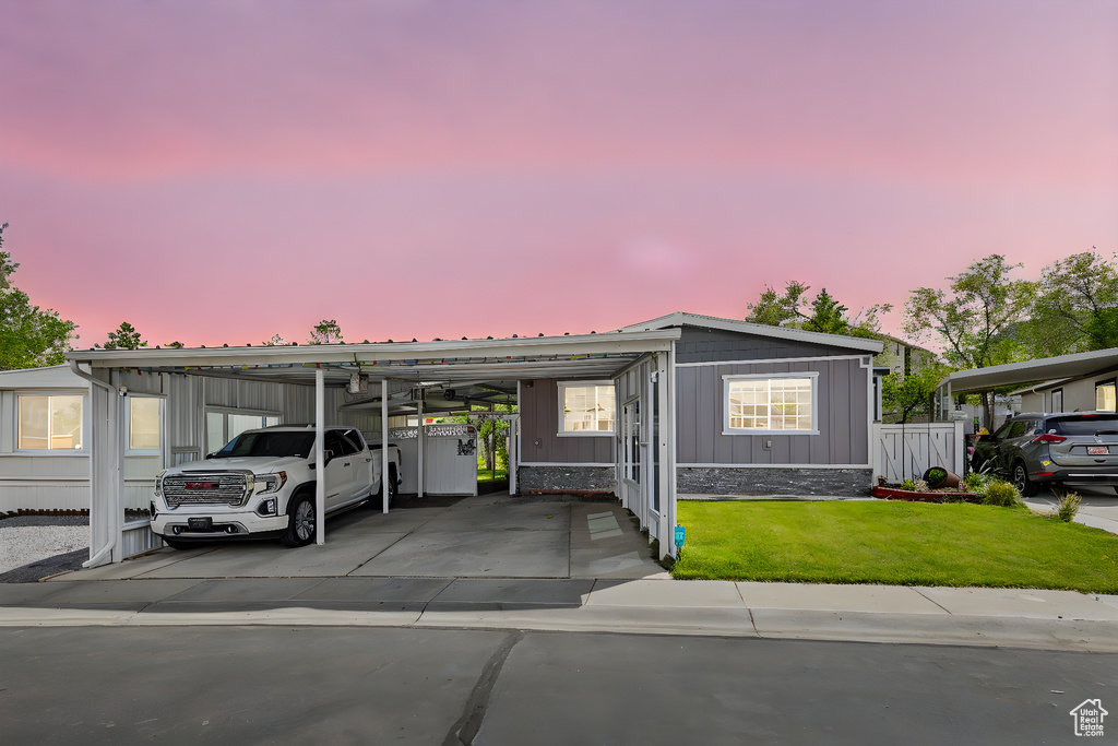 Manufactured / mobile home with board and batten siding, driveway, a lawn, a carport, and fence