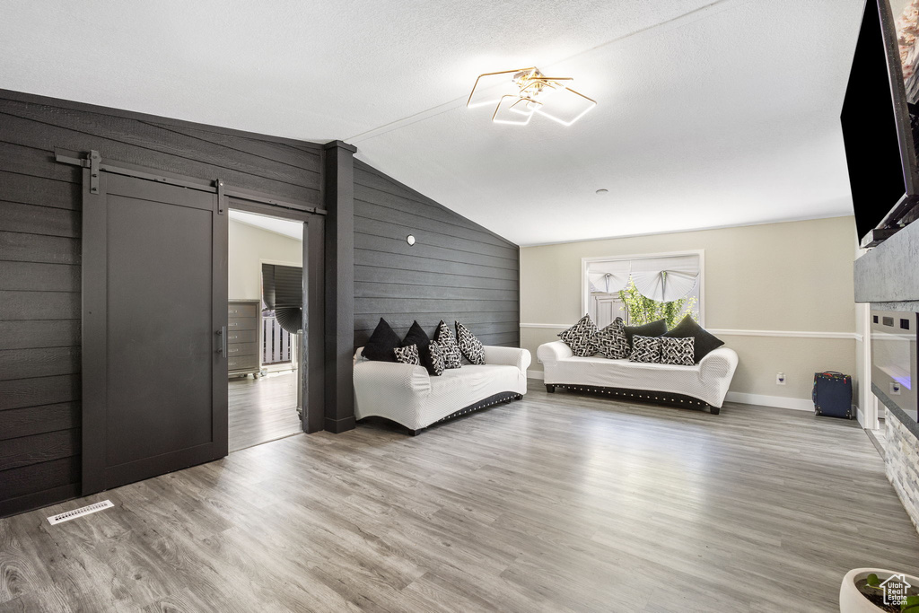 Living area featuring wooden walls, vaulted ceiling, wood finished floors, and visible vents