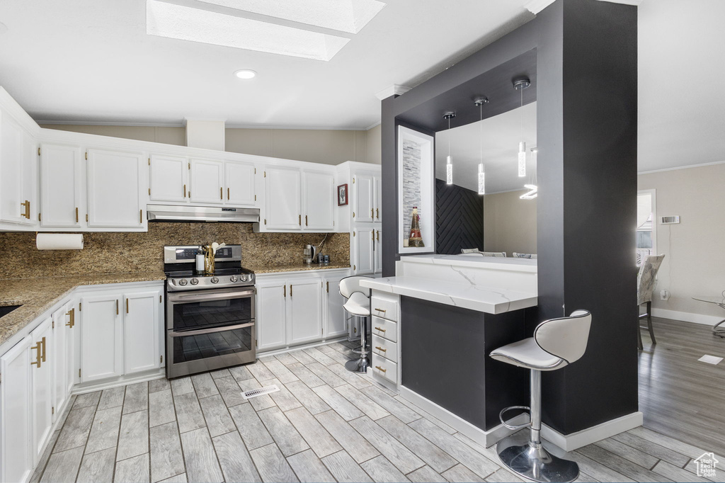 Kitchen featuring double oven range, a skylight, tasteful backsplash, light wood-style floors, and under cabinet range hood