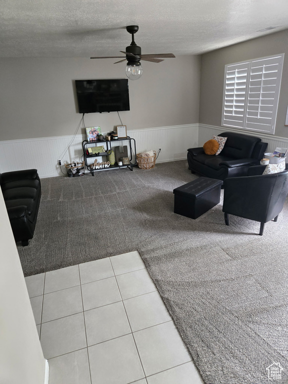 Living room featuring a textured ceiling, ceiling fan, wainscoting, and light colored carpet