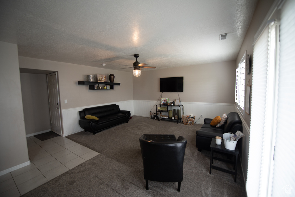 Tiled living room featuring carpet flooring, ceiling fan, a textured ceiling, a wainscoted wall, and visible vents