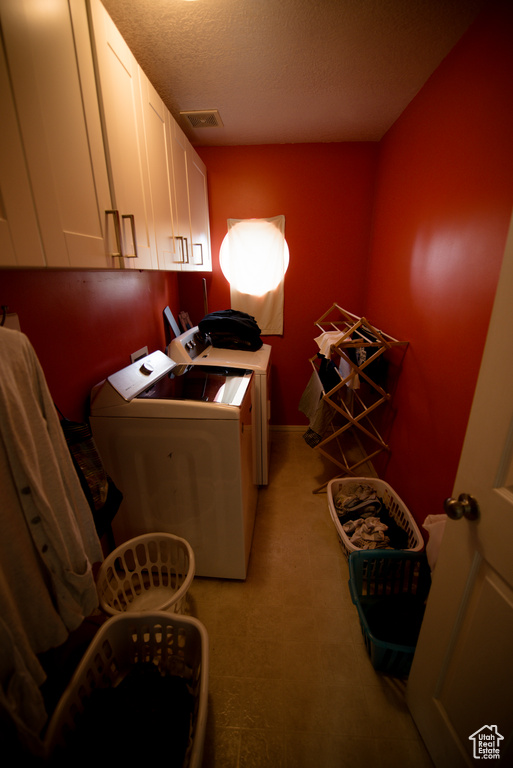 Clothes washing area with visible vents, a textured ceiling, cabinet space, and independent washer and dryer