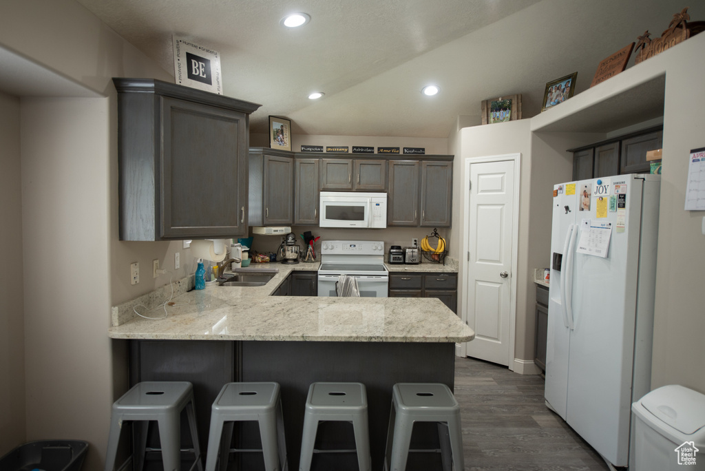 Kitchen with a sink, a peninsula, dark wood-style floors, recessed lighting, and white appliances