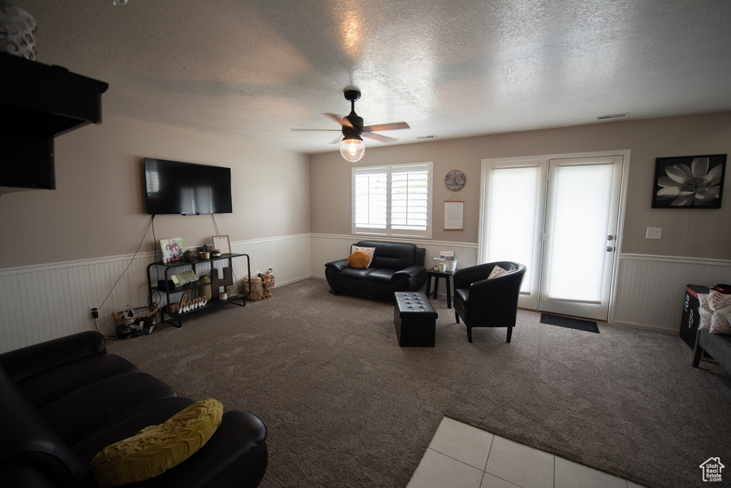 Living room with carpet floors, a ceiling fan, a textured ceiling, and a wainscoted wall