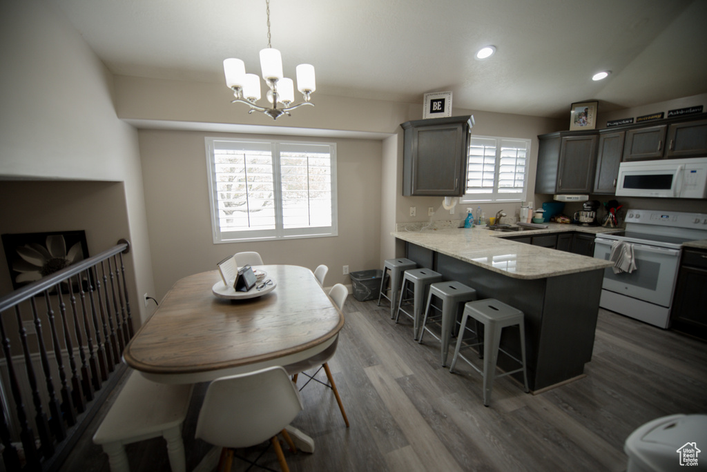 Kitchen with a sink, white appliances, a kitchen breakfast bar, a chandelier, and a peninsula
