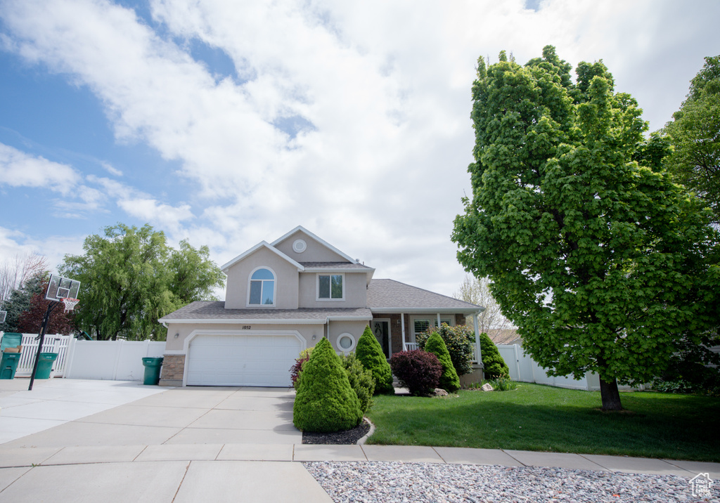 View of front facade featuring a garage, fence, a front lawn, concrete driveway, and stucco siding