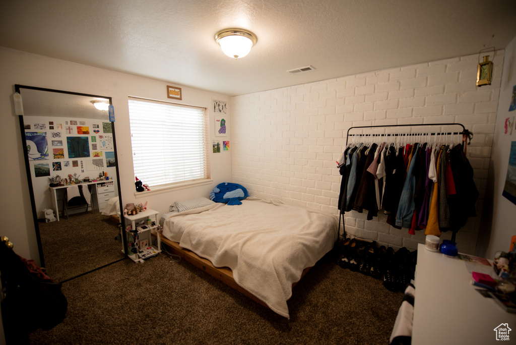 Bedroom featuring carpet floors, a textured ceiling, brick wall, and visible vents