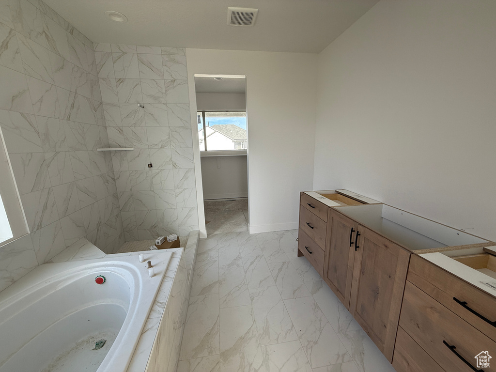 Bathroom with marble look tile flooring, a garden tub, tiled shower, and vanity