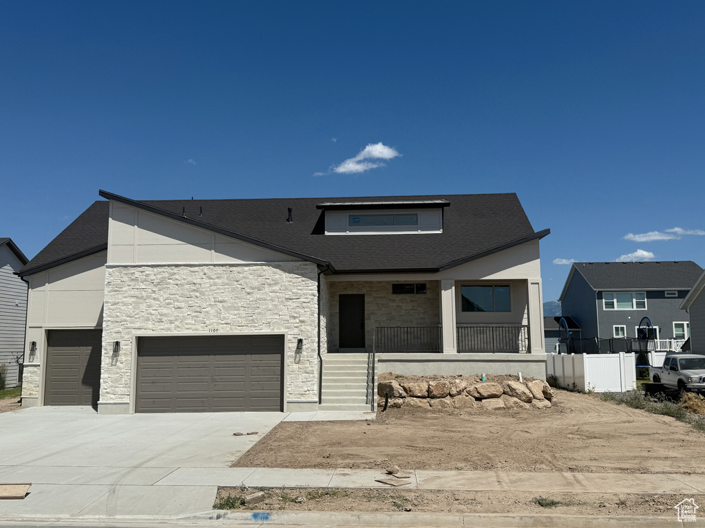 Modern home featuring covered porch, stone siding, concrete driveway, and a garage