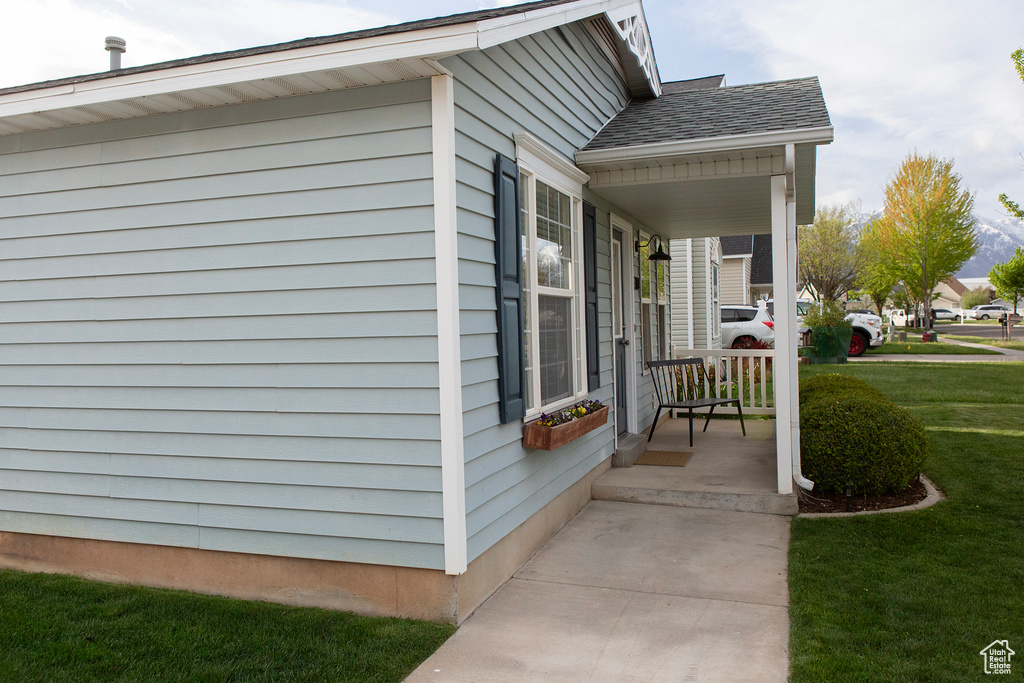 View of home's exterior featuring a lawn, covered porch, and a shingled roof