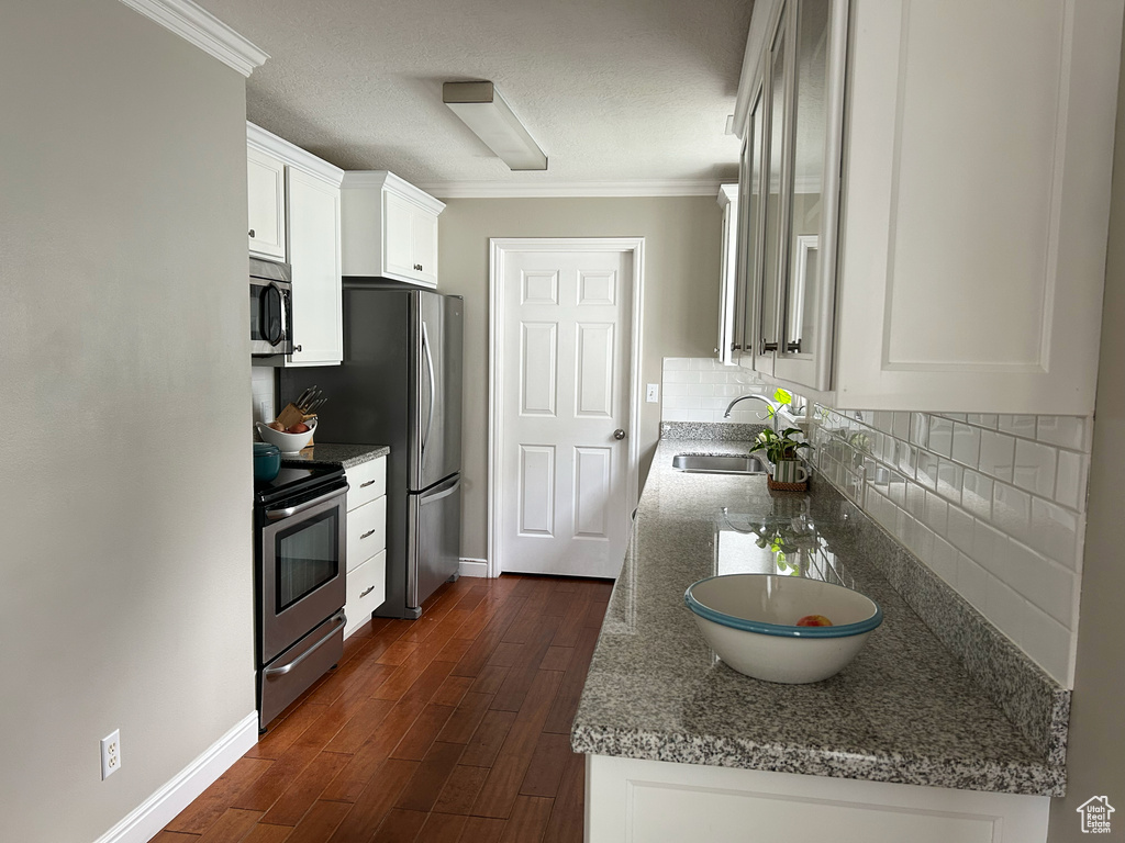 Kitchen featuring a sink, stainless steel appliances, baseboards, ornamental molding, and backsplash